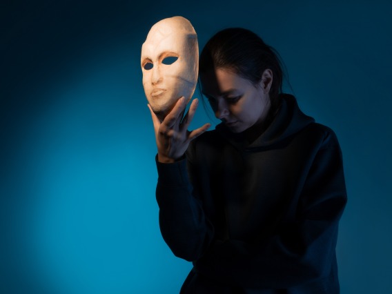 A woman holds a mask in front of her face