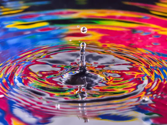 Water droplet falling into a pool of water with a colorful reflection