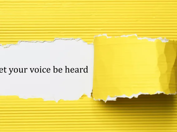 Yellow paper peeled away to reveal text "Let your voice be heard" on a white background