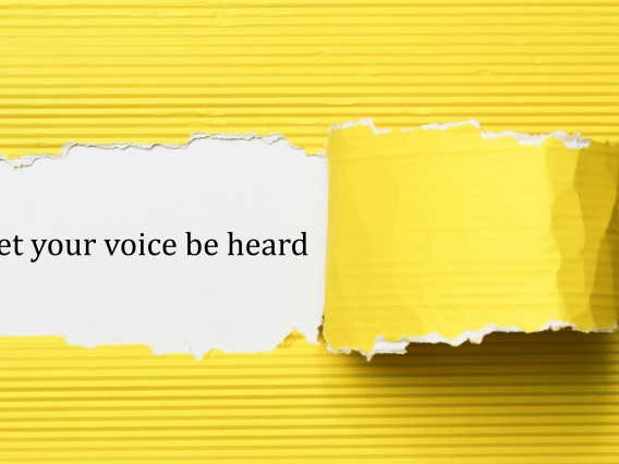 Yellow paper peeled away to reveal text "Let your voice be heard" on a white background
