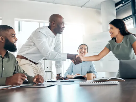 Four people at a business meeting, two are shaking hands.