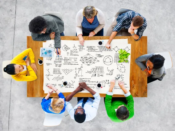 8 people sitting around a table drawing geometry diagrams.