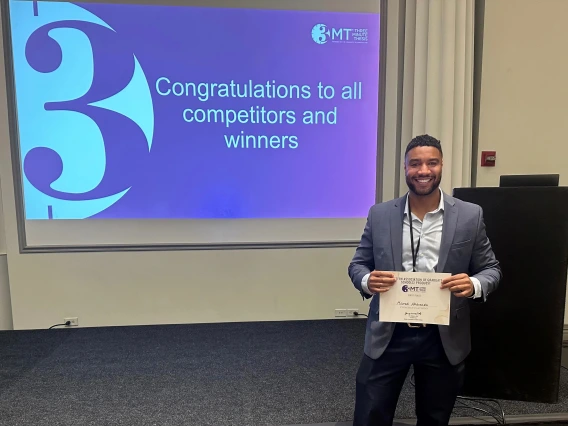 Mourad Abdennebi stands holding his certificate in front of a projected slide reading "Congratulations to all competitors and winner" 