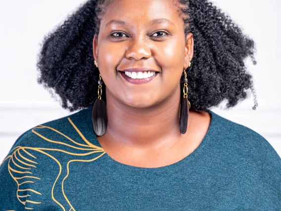 Smiling woman with black curly hair, wearing a green top and long earrings in front of a white background