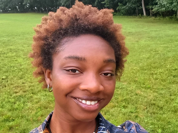 Portrait of Safiyyah Ogundipe in a green field near woods.