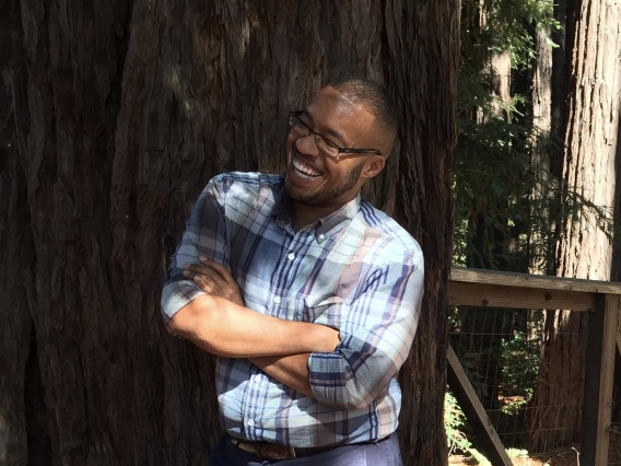 A smiling Sy Simms leaning against a tree.