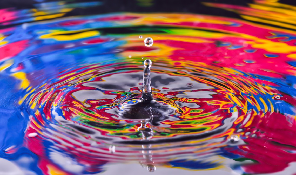 Water droplet falling into a pool of water with a colorful reflection