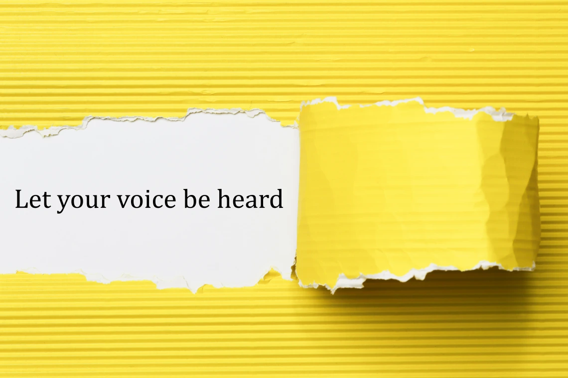 Yellow paper peeled away to reveal text "Let your voice be heard" on a white background