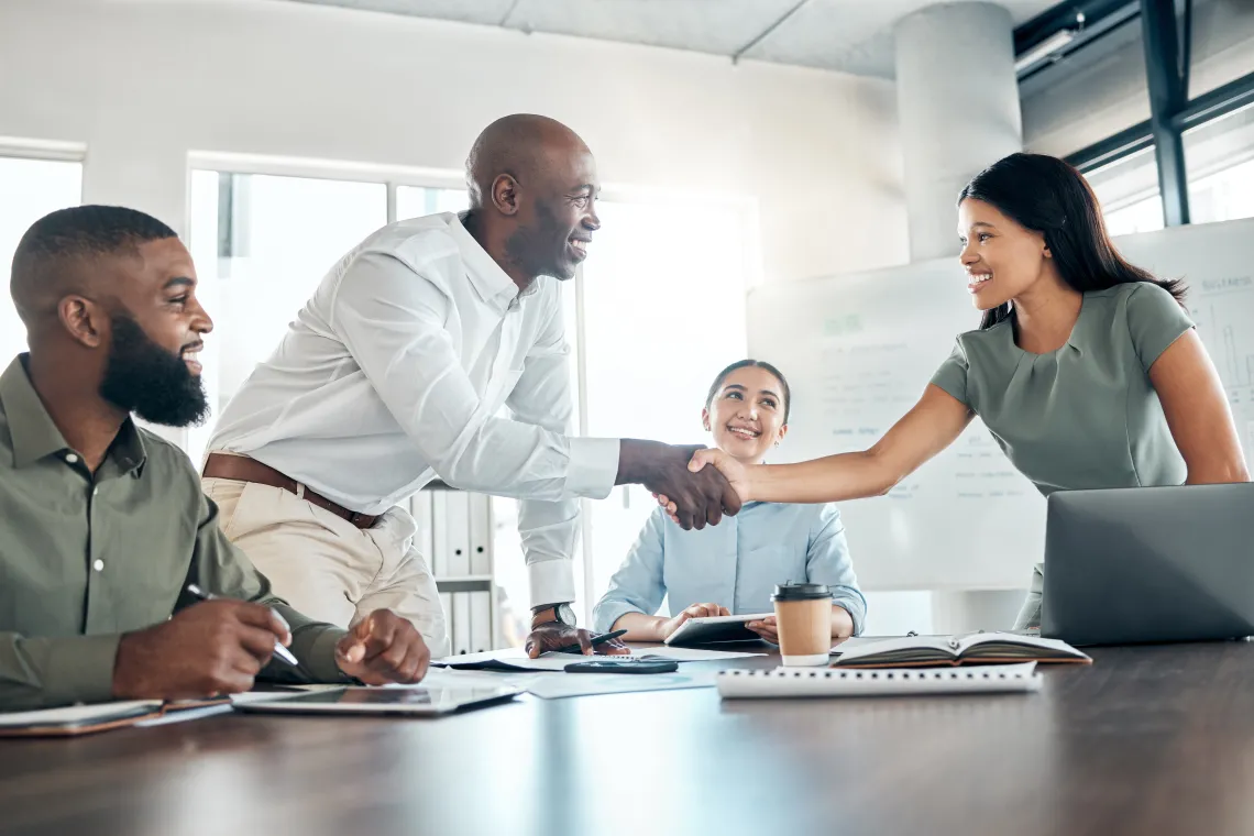 Four people at a business meeting, two are shaking hands.