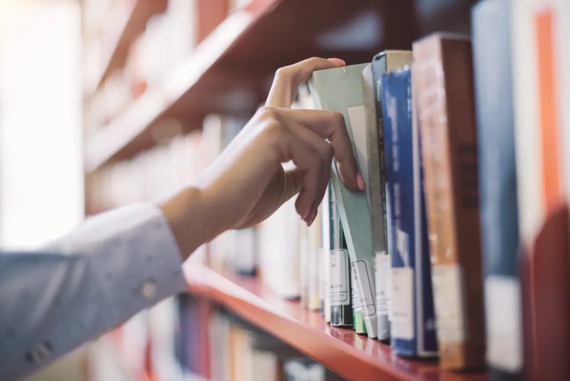 Hand pulling book off of library shelf.