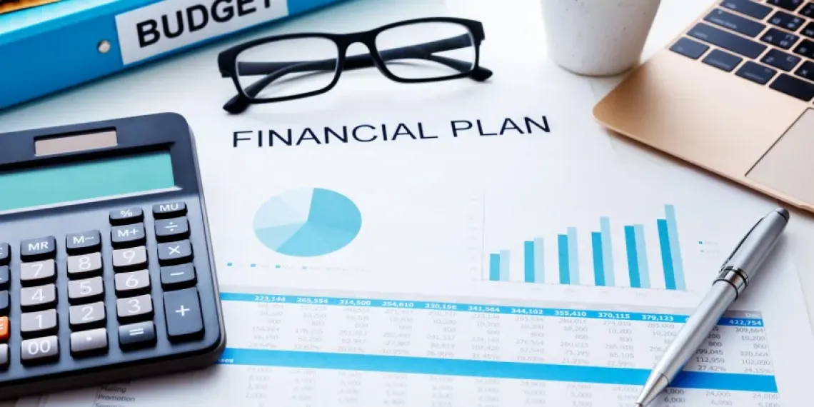 A document titled Financial Plan surrounded by a laptop, pen, glasses, calculator, and a binder.