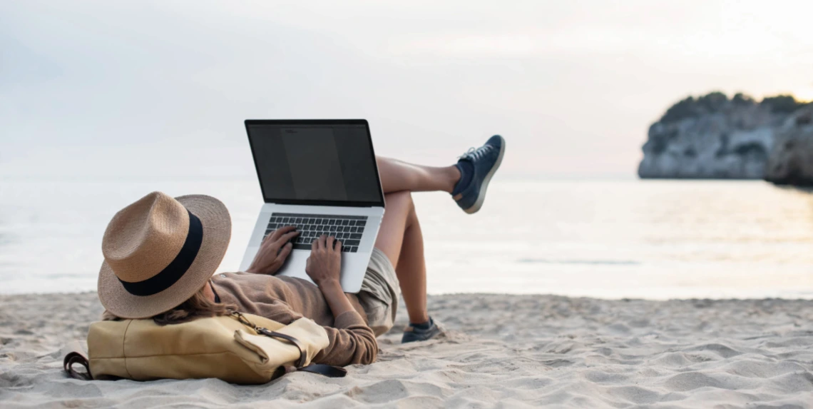 Image of a man on a beach typing on a laptop computer.