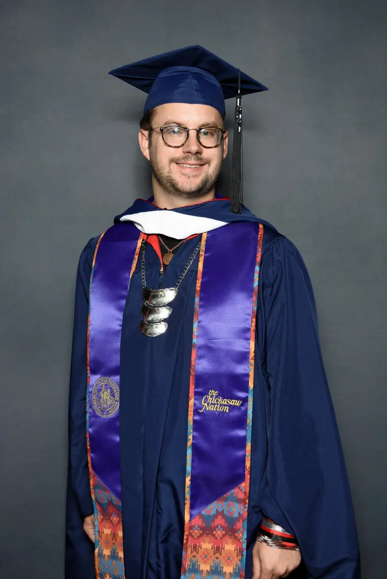 Portrait of Andrew McNair wearing graduation regalia and tribal regalia.