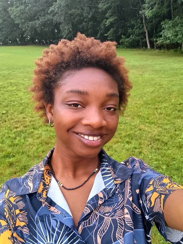 Portrait of Safiyyah Ogundipe in a green field near woods.