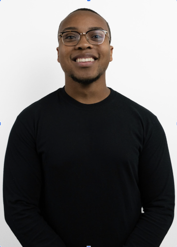 A professional headshot of an African American individual in a black sweater on a white background.