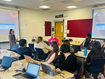 Image of several students in a class room on computers writing. Karla Smith stands at the front of the room. 