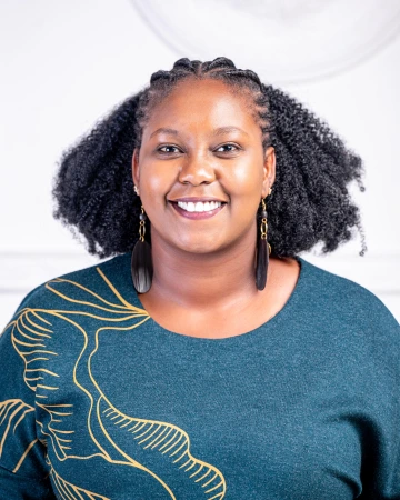 Smiling woman with black curly hair, wearing a green top and long earrings in front of a white background