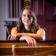 Greta Pasztor facing the viewer while sitting at an open piano