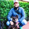 Josh in a cap and jacket crouching next to a brown dog with a pink leash