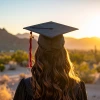 Student wearing graduation cap facing sunset and mountains